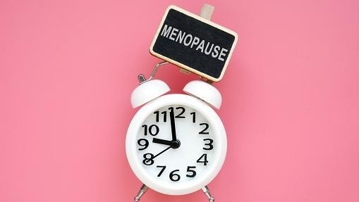 Alarm clock and word menopause on a pink background.